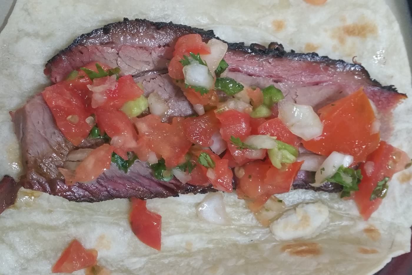 Sliced smoked brisket with fresh pico de gallo on a tortilla