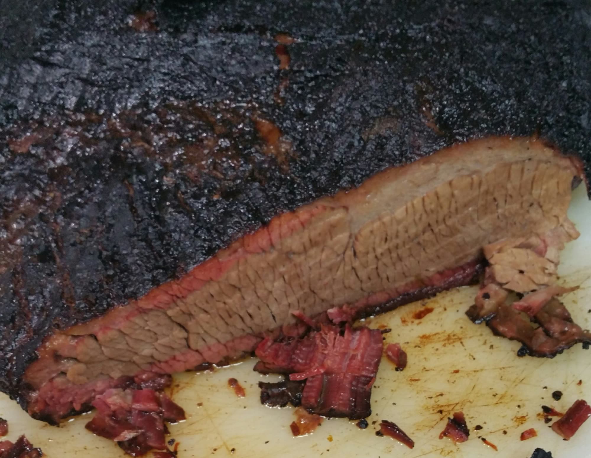 A smoked brisket with a dark peppery bark, sliced on the board